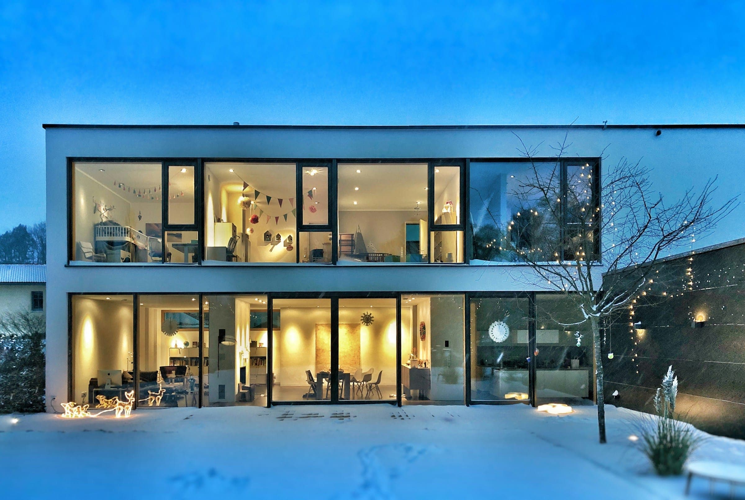 Maison contemporaine aux larges baies vitrées éclairées à la tombée de la nuit